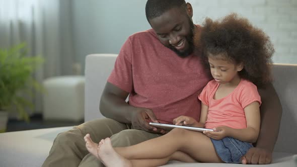 Dad and daughter having fun together playing educational games on tablet