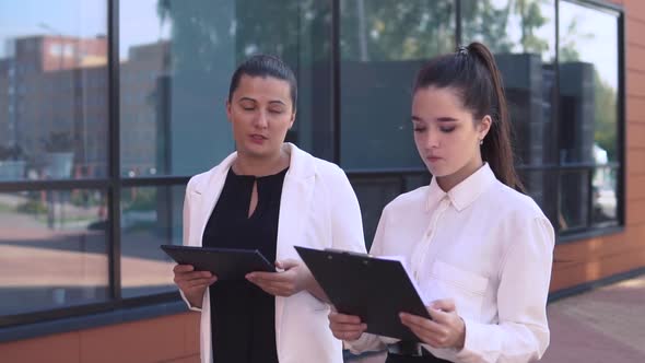 Two Business Girls Walking Down the Street and Discussing a Working Project