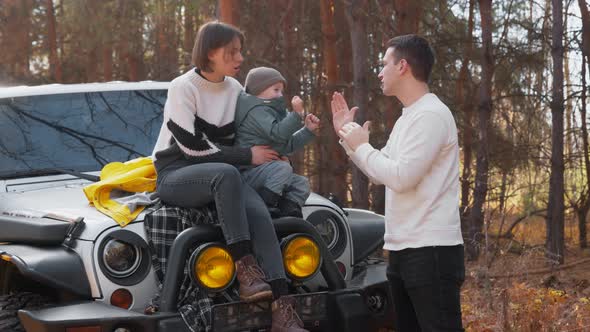 Young Happy Mother Sits on Car with Her Son and Young Father Plays with Him in Autumn Forest