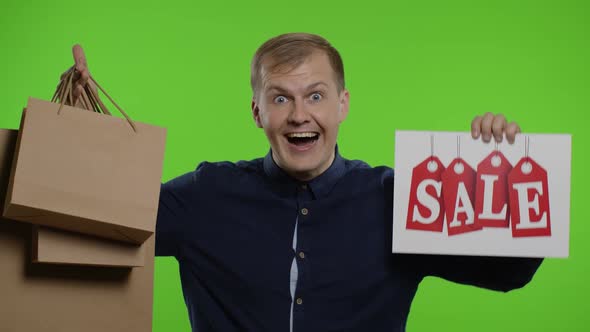 Surprised Guy Showing Shopping Bags and Sale Word, Looking Astonished By Low Cost Purchase, Discount