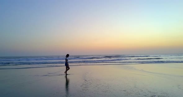 Aerial drone view of a young woman walking on the beach at sunset.