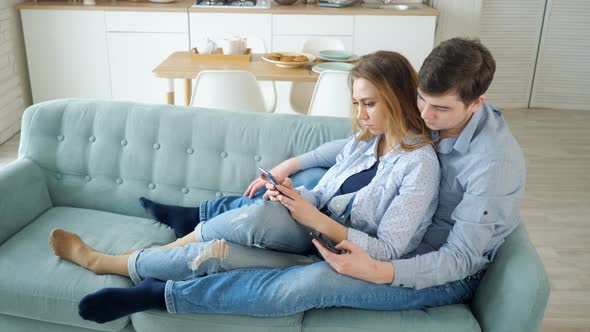 Guy and Girl Sit on Sofa Surfing Internet in Smartphones