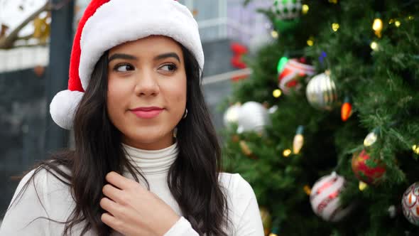 An attractive woman in a Santa hat on the naughty list in front of a Christmas tree with ornaments a