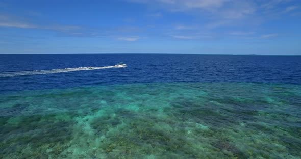 Aerial drone view of man and woman on an inflatable tube towing behind a boat to a tropical island.