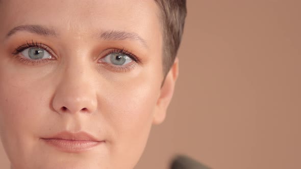 Caucasian Woman with Short Haircut and Natural Beige Makeup in Studio on Beige Background