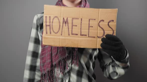 A untidy beggar woman begging and holds a cardboard sign with the inscription homeless