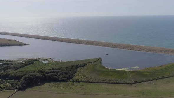 Aerial tracking forward from inland towards the fleet lagoon at Abbotsbury in Dorset. Chesil beach a