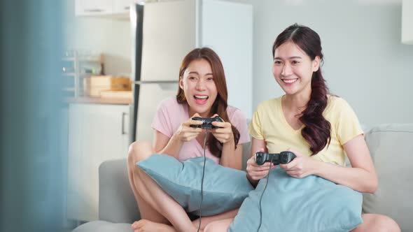 Two female gay lesbian friend sit on sofa in living room, feel happy to play joystick game at home.