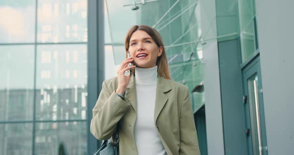 Caucasian Woman Speaking on Mobile Phone Walking Beside Office Outdoors