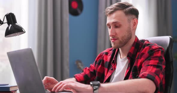 A Handsome College Student Boy is Studying Remotely While Sitting at a Desk in Living