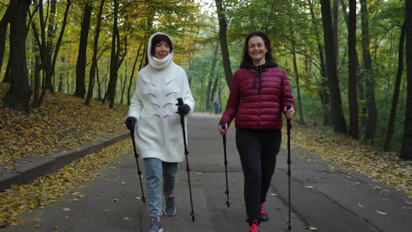 Dolly Shot Portrait of Two Confident Athletic Mature Women Strolling with Poles for Nordic Walking