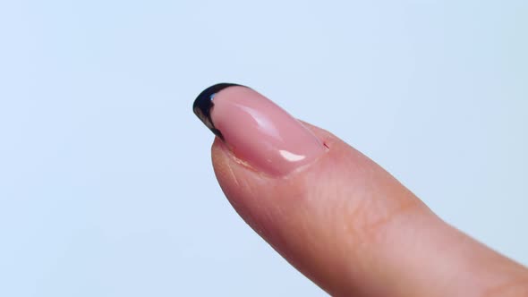 close-up of a manicurist paints a black French on the client's nails with a brush.