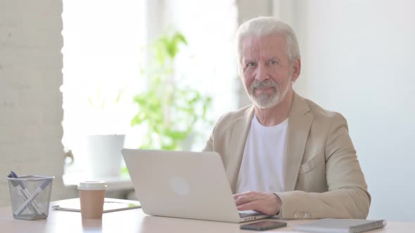 Old Man Shaking Head in Approval While Using Laptop in Office