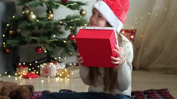 Little Girl in Santa Hat Shakes Christmas Gift Trying to Understand What is in Package