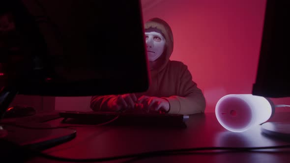 Anonymous Person in a White Mask Works on the Computer Inputs Code Types Very Fast on the Keyboard