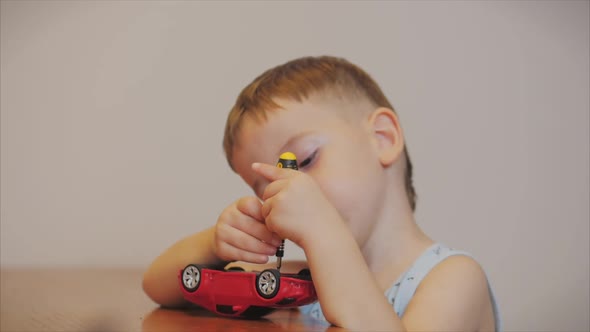 Shooting a Portrait of a Cute Preschool Boy, the Child Repairs His Favorite Red Toy Car for Kids