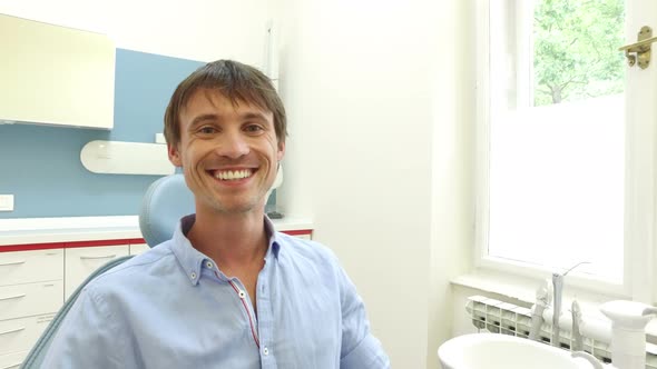 Young man with healthy white teeth smiling and looking at camera at dentist