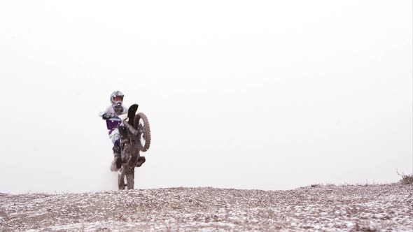 Motorcycle jumps over the camera in the falling snow.