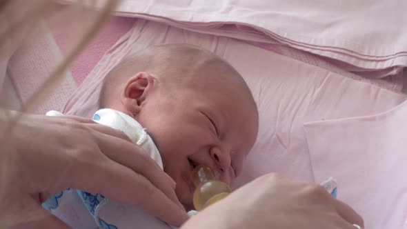 Mother giving bottle with water to sleepy newborn baby