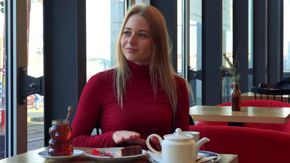 A Young Attractive Woman Sits at a Table with Meal in a Cafe and Dances with a Smile