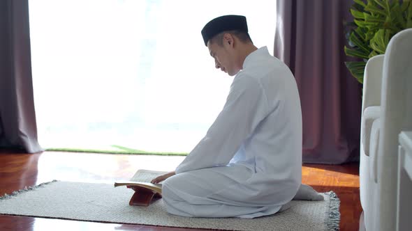 Young Muslim man wearing Islamic clothes reading the Quran