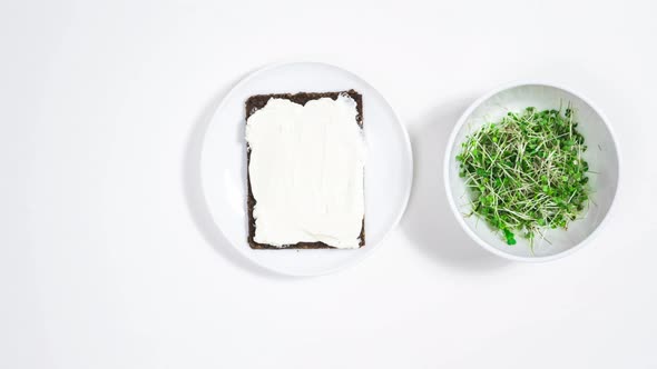 Sandwich is spread with cream cheese and topped with green shoots