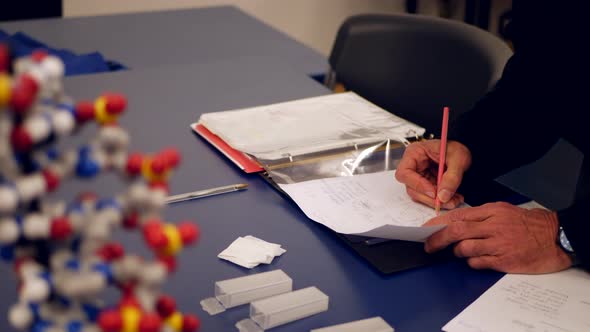 A college science professor grading homework assignments from his students and taking notes in his b