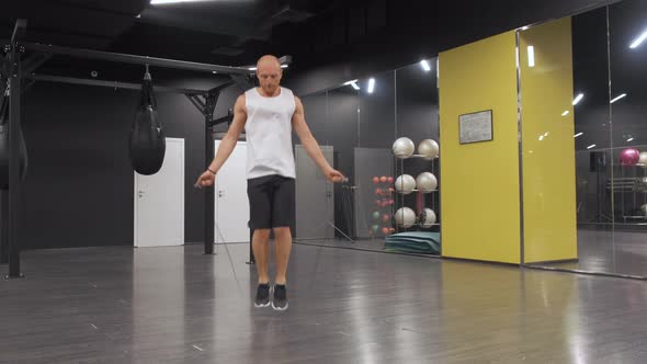 Male boxer with skipping rope. Fighter doing jump rope exercises in dark gym