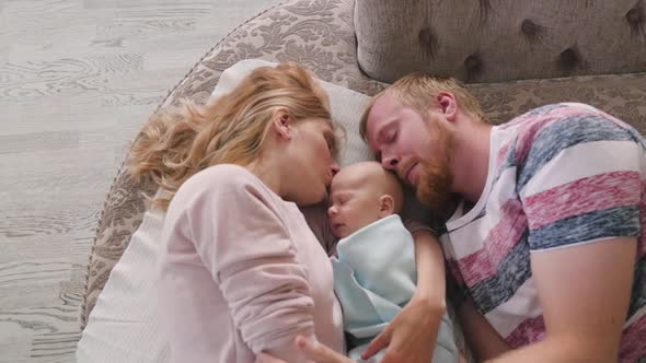 Happy Young Family with a Newborn Baby. Mom, Dad and Newborn Lying on the Bed, Top View. Happy Mom