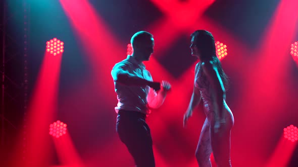 Young Sexy Couple Dancing Salsa. Woman in a Skin-tight Suit and a Man in a White Shirt and Black