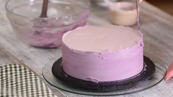 The process of decorating a cake with purple cream cover. 