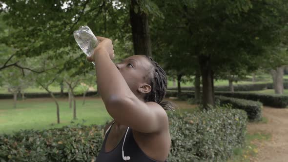 thirsty black female athlete drinks water in the park-slow motion