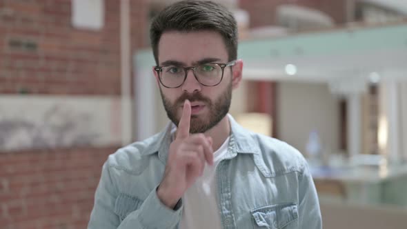 Portrait of Sneaky Young Male Designer Putting Finger on Lips