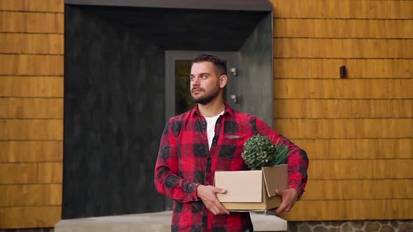 Smiling Bearded Man With Box in His Hands Standing Near Beautiful House and Posing on Camera