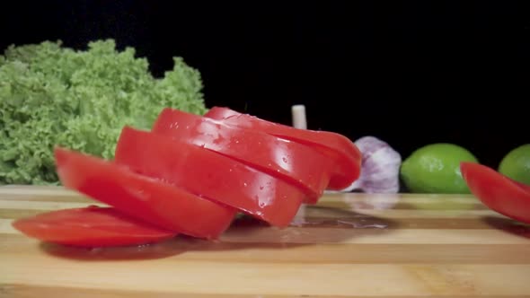 Rings of a Red Tomato Wet in Drops of Water Falling on Wooden Board