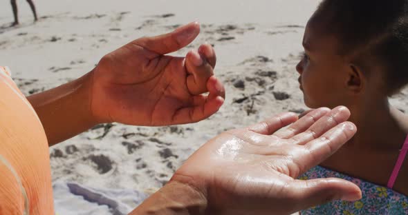 Smiling african american family using sun cream on sunny beach