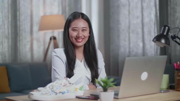 Female Footwear Designer Smiling And Crossing Her Arms To The Camera While Working On A Laptop