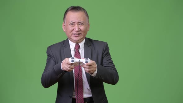 Mature Japanese Businessman Playing Games Against Green Background