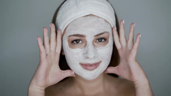 Young Woman with Cosmetic Mask on Face Looks and Poses at Camera on Background