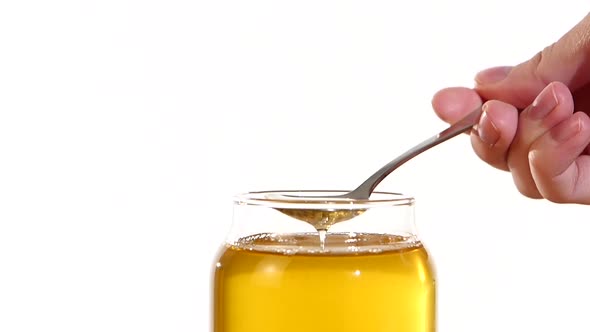 Hand Taking Honey From Glass Jar Using Metal Spoon, on White, Slow Motion