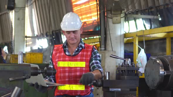 Male factory foreman using laptop checking on metal machine in the factory