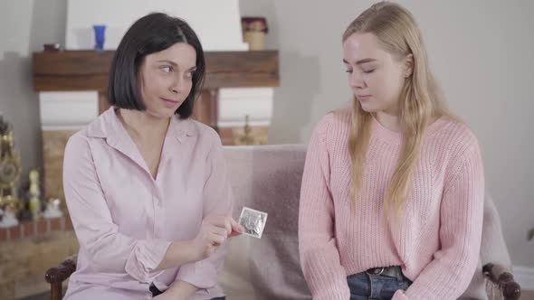 Young Brunette Caucasian Mother Giving Her Teenage Daughter Condom. Wise Woman Taking Care of Her