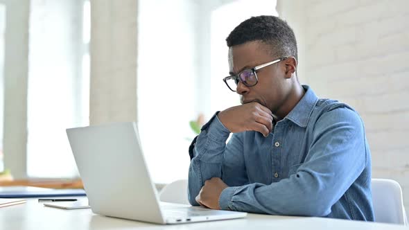 Young African Man Thinking and Working on Laptop