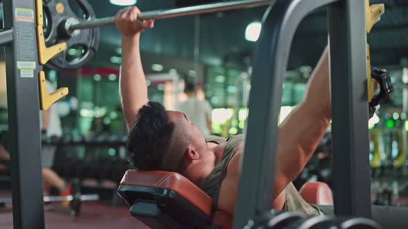 Asian sportsman workout exercise by slowly lift up weight machine or barbell in fitness stadium.