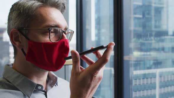 Caucasian man wearing face mask talking on smartphone at modern office