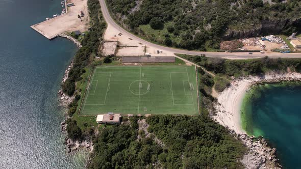 Moving away shot of Soccer field on cliffed headland in greece. Street along coastline visible. Reve