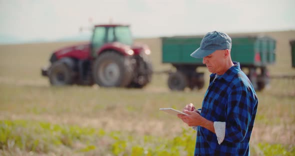 Farmer Using Digital Tablet While Looking at Tractor in Farm