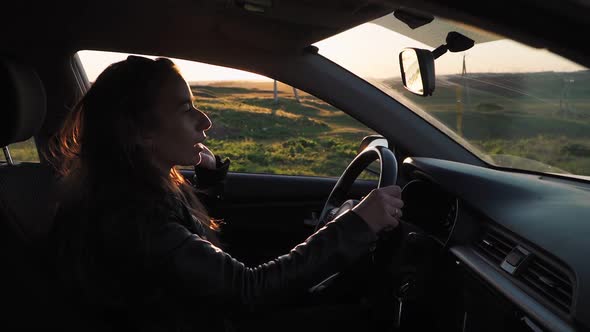 Young woman driving the car outside the window beautiful sunset landscape