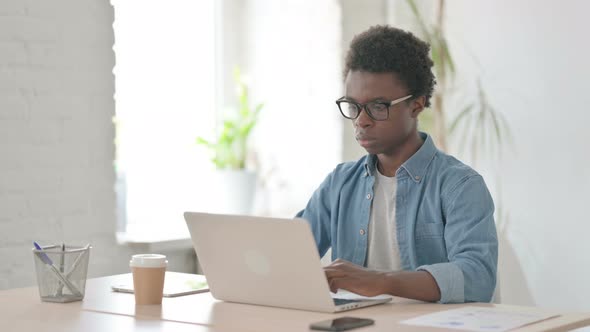 Busy Young African Man Using Laptop in Office