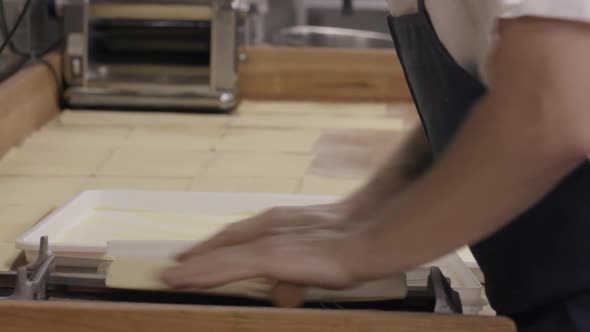 A skilled pasta chef rolls out pasta noodles by hand in the kitchen of a high end restaurant